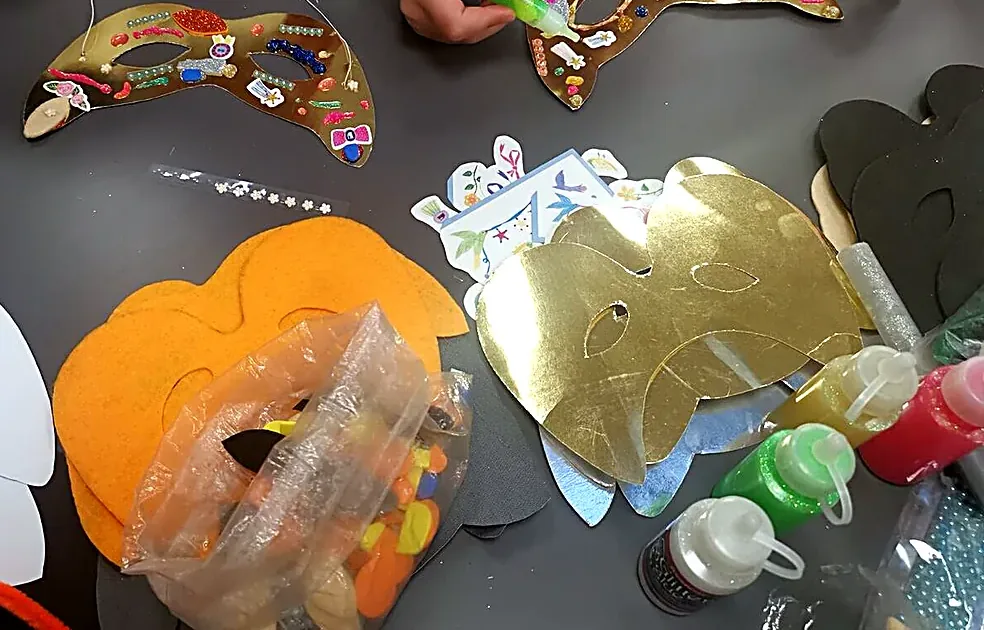 Mascherine di carnevale a forma di gatto, dorate e arancioni, sul tavolo del laboratorio